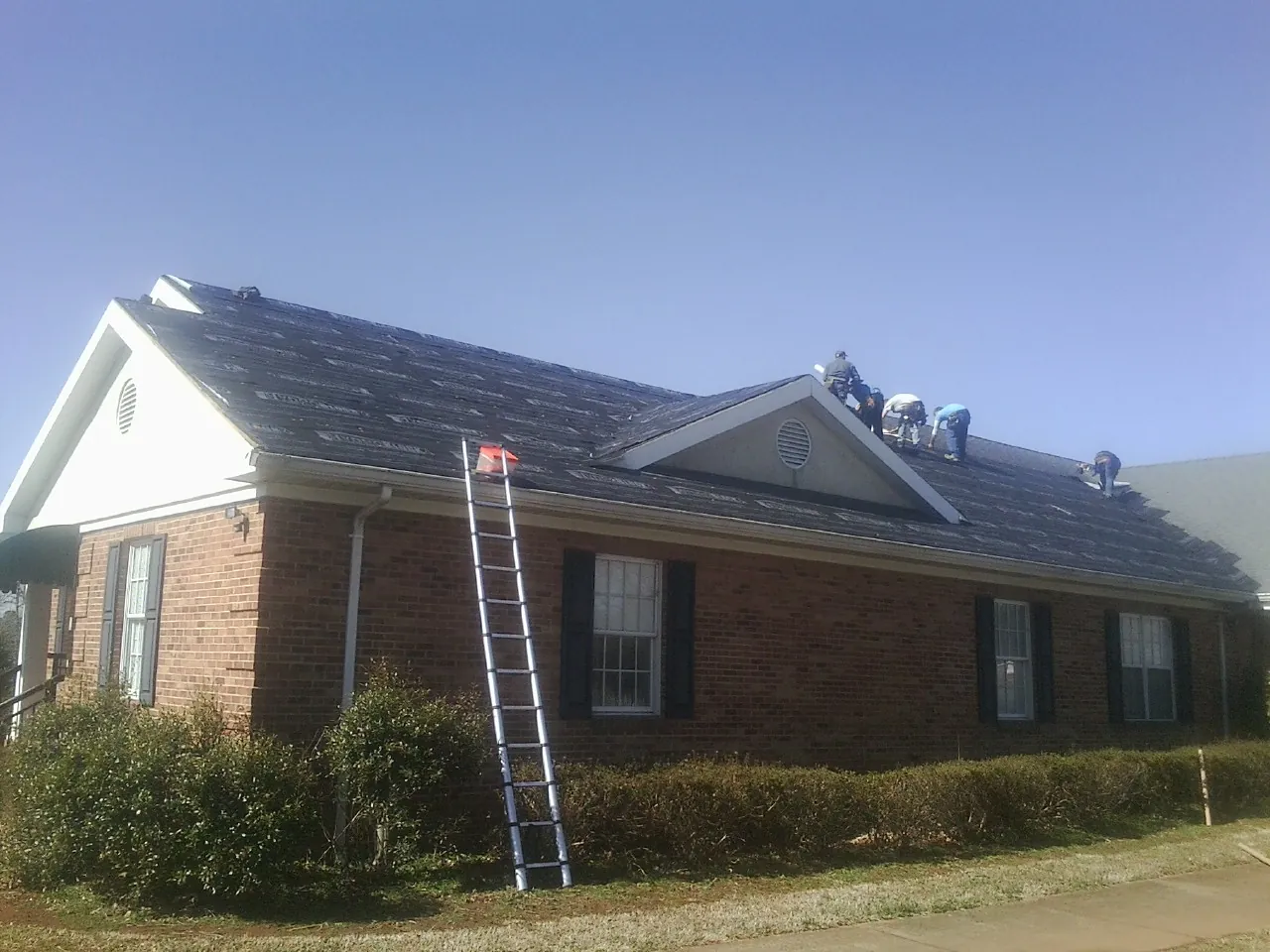Crew tearing shingles off a brick ranch roof with a ladder set — Emergency Roof Repair work by our crew in Finger