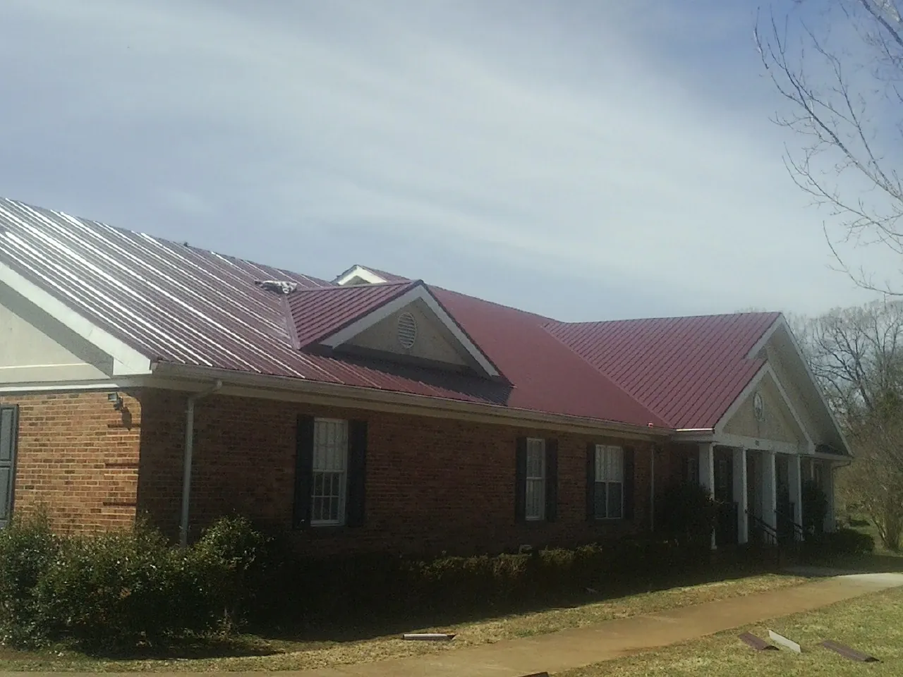 Red metal roof with gabled entries on a long brick building, from a Hail Damage Roof Repair job in Finger