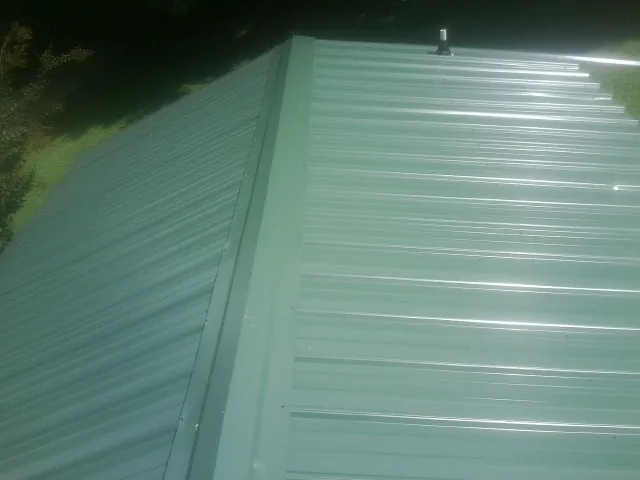 New green metal panels meeting at the ridge of a roof — Flat Roof Repair work by our crew in Finger