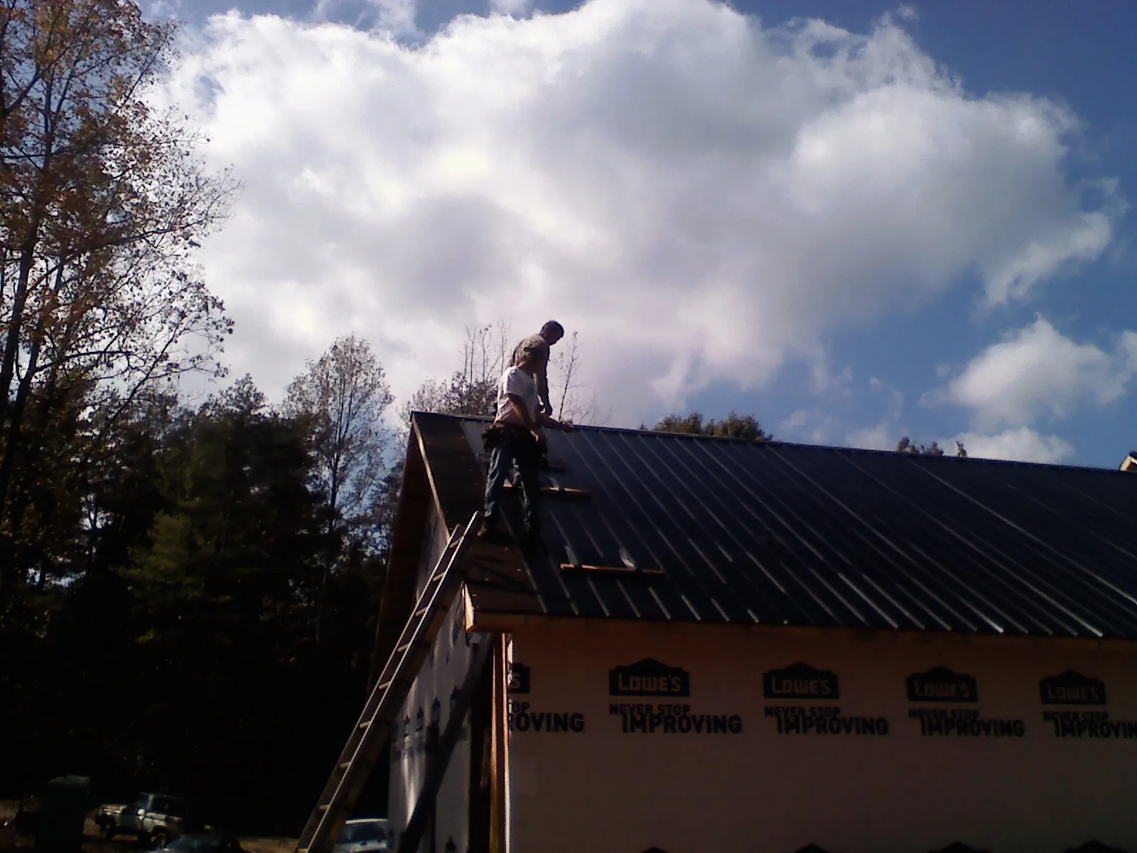 Roofer fastening dark metal panels high against a cloudy sky, from a Roof Inspection job in Finger