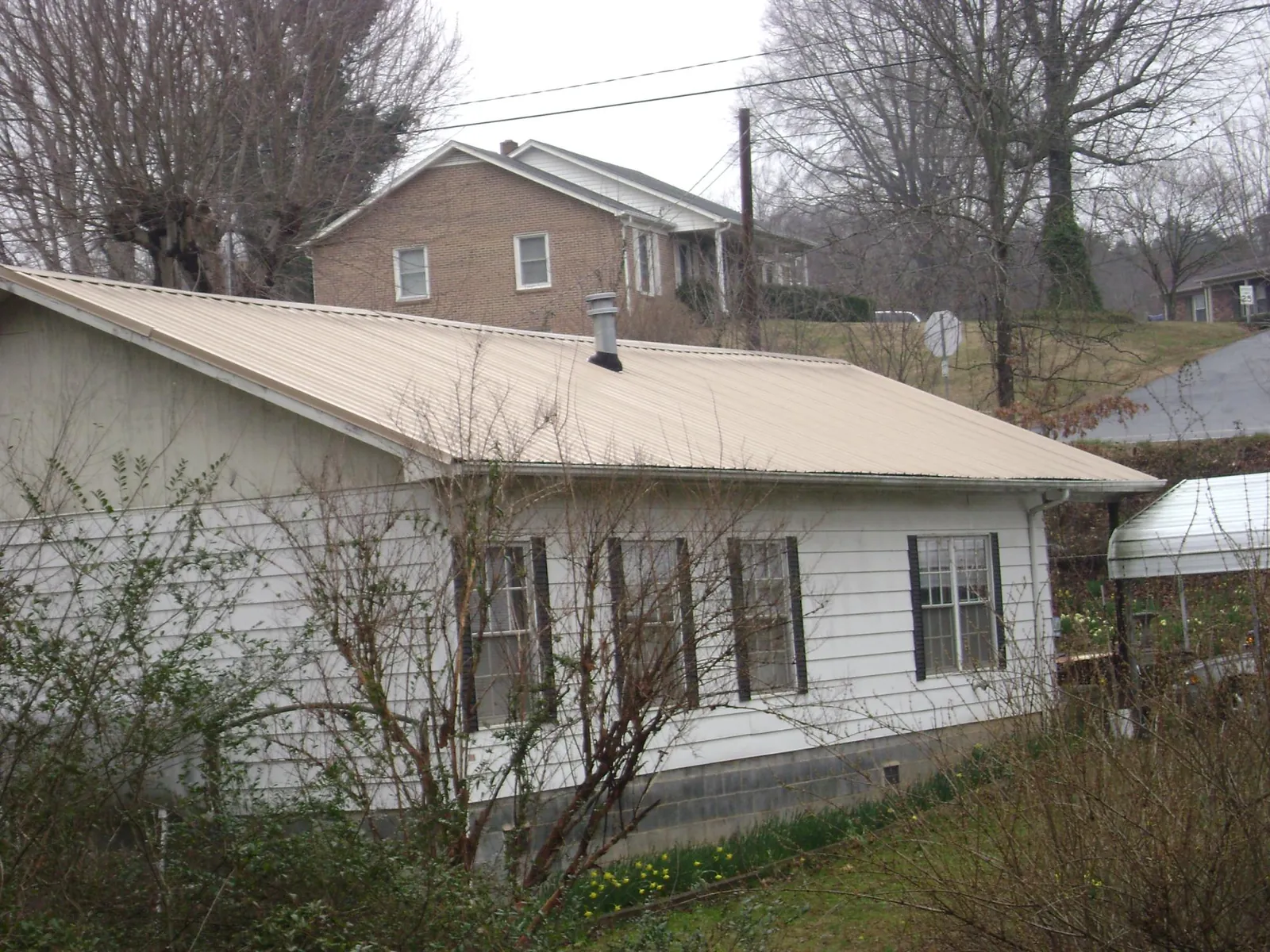 Tan metal roof on a white sided house set into a hillside — Commercial Roofing by Roofing Brothers in Finger