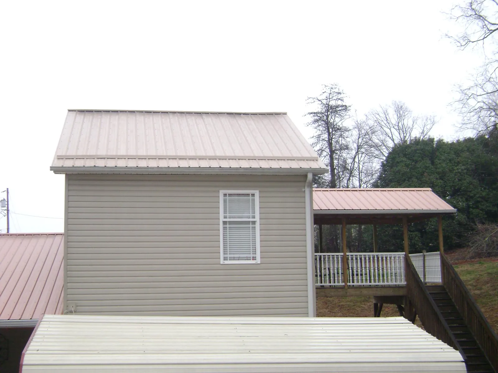 Tan metal roofs on a two story addition and attached porch, from a Roof Replacement job in Finger